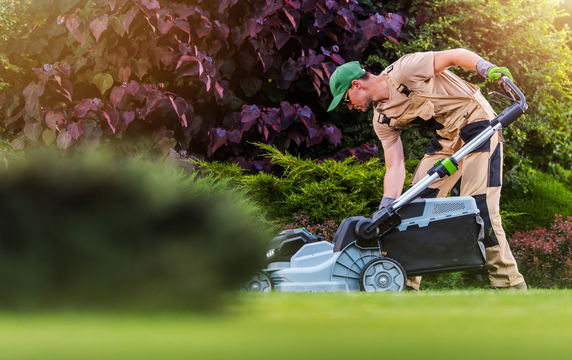 A gardener from a local lawn care company mowing a backyard lawn with an electric grass mower.
