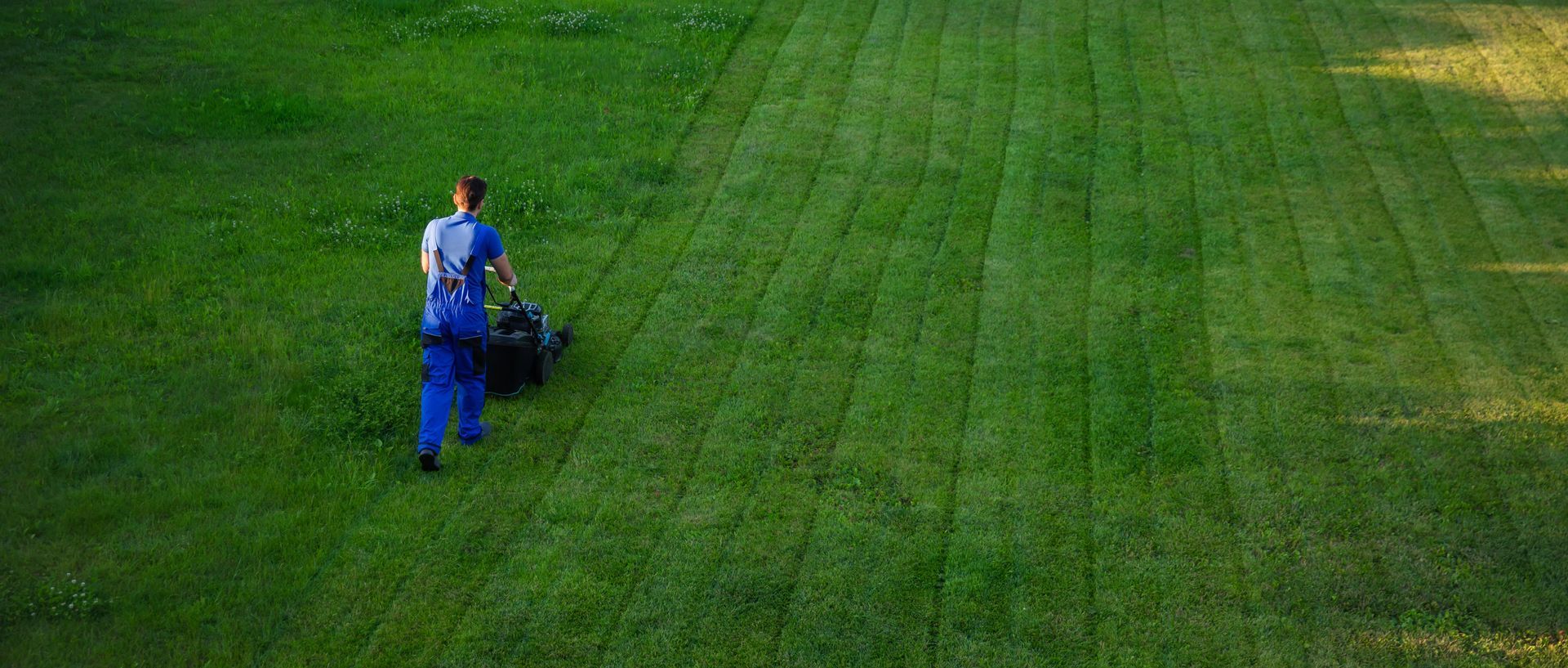 Person mowing large green lawn with striped pattern. Person mowing large green lawn with striped pattern.