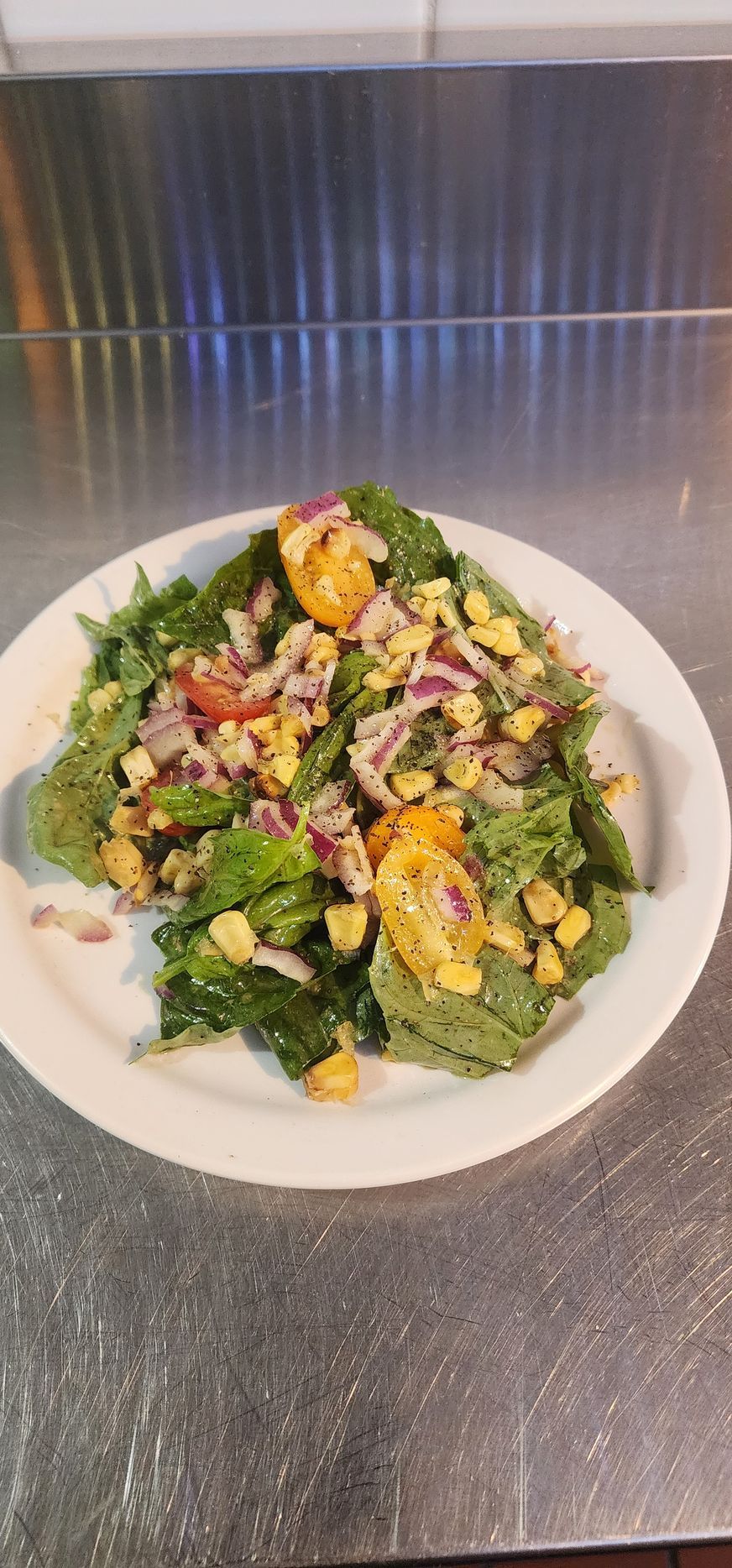 A salad plate with basil and corn on a stainless steel table top