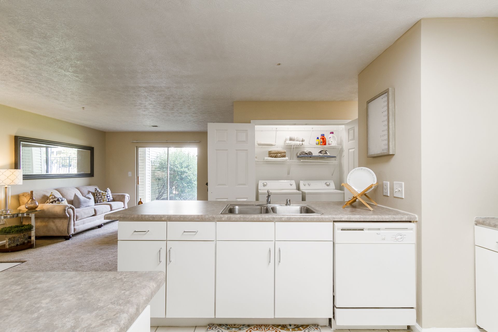 Kitchen with white cabinets, open to living room with couch, laundry room visible. Visit Bridle Creek to explore our 2-bedroom apartments for rent in Lexington, KY.