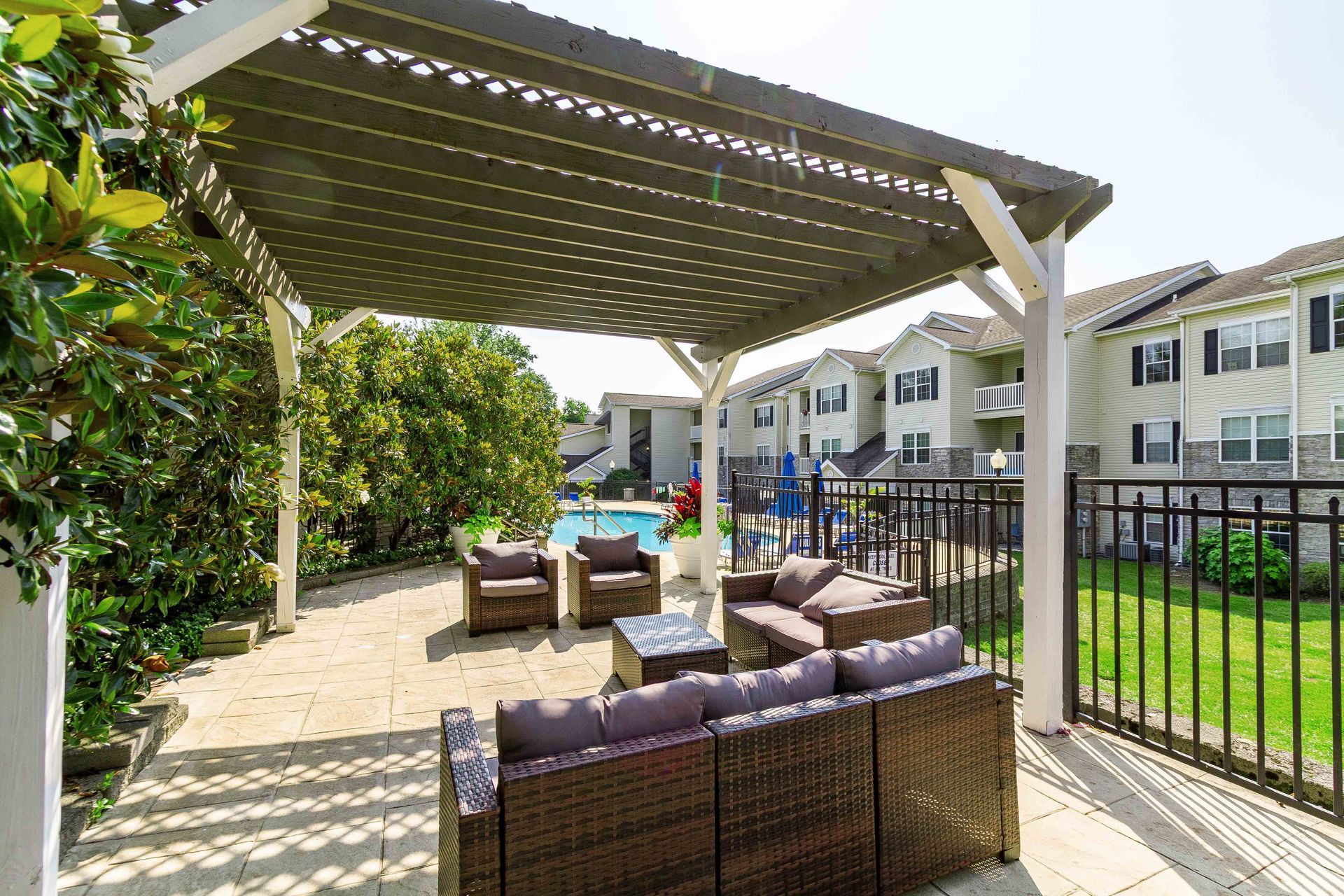 Patio with shaded seating, pool, and apartment buildings in the background. Visit our community to view Apartments for rent in Lexington, KY firsthand.