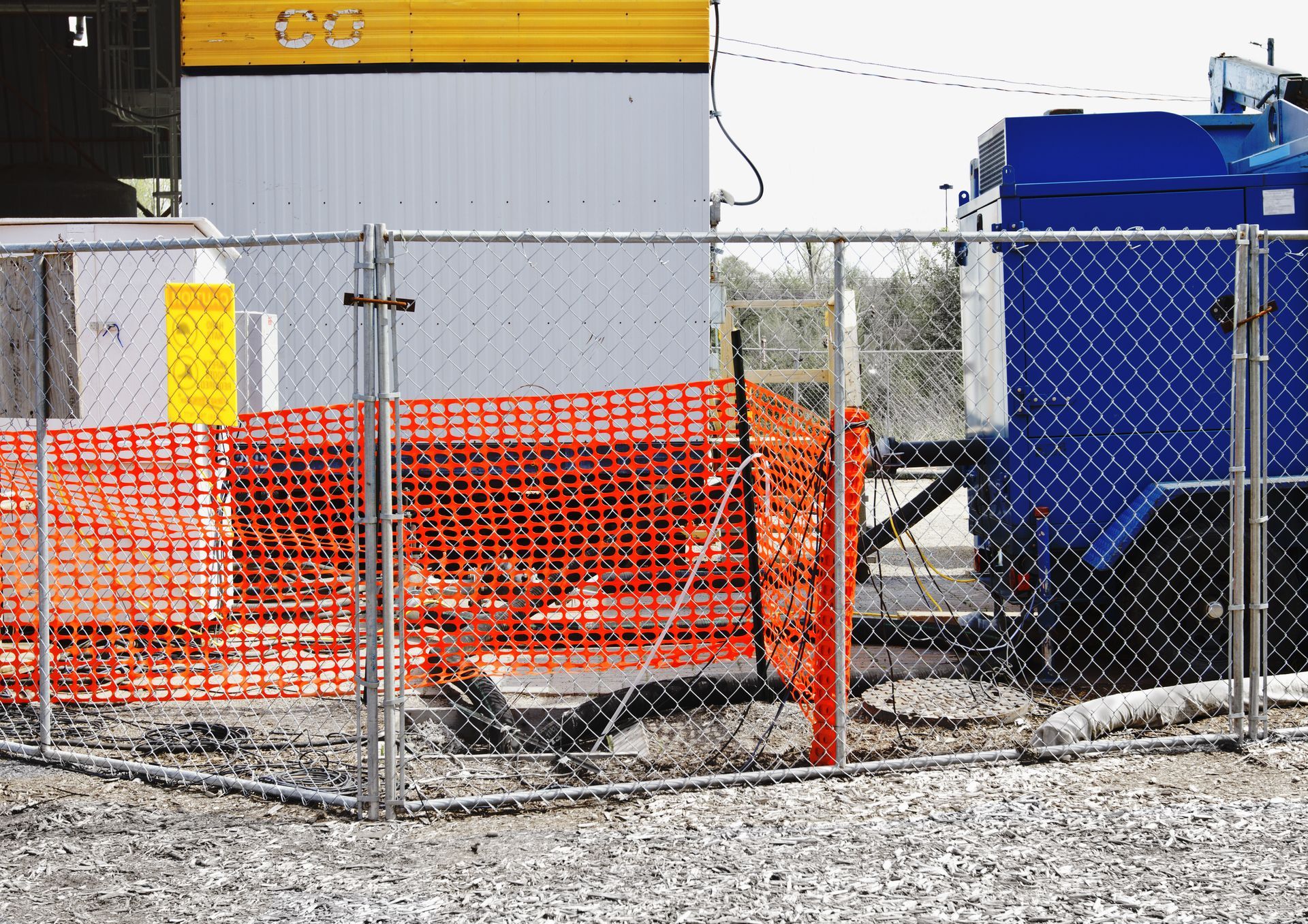 a chain link fence surrounds a construction site with a blue dumpster in the background
