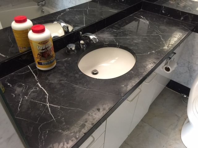 Black marble bathroom countertop with white sink, chrome faucet, and cleaning products.