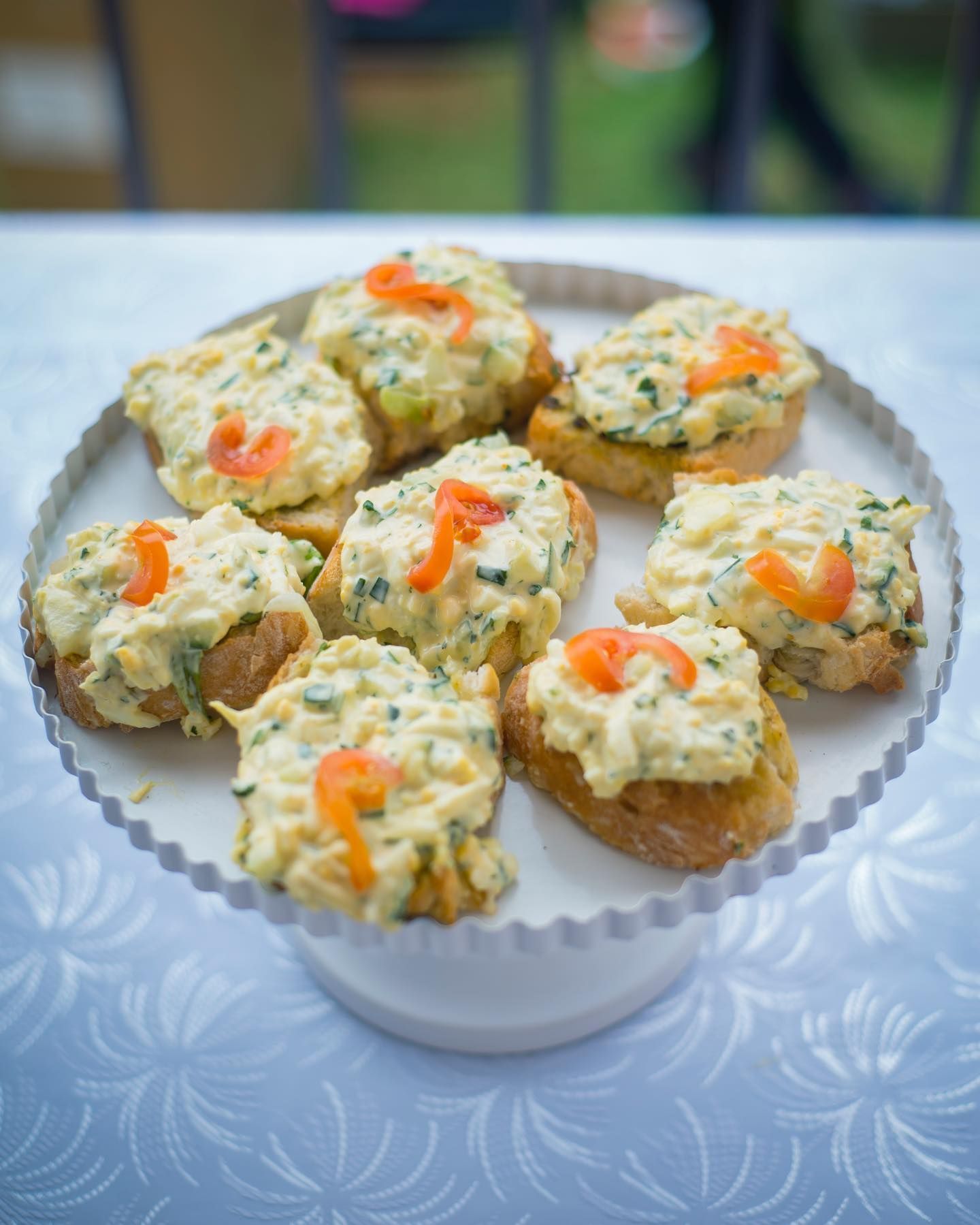 A plate of food with egg mayo on a bagette on top of it on a table.
