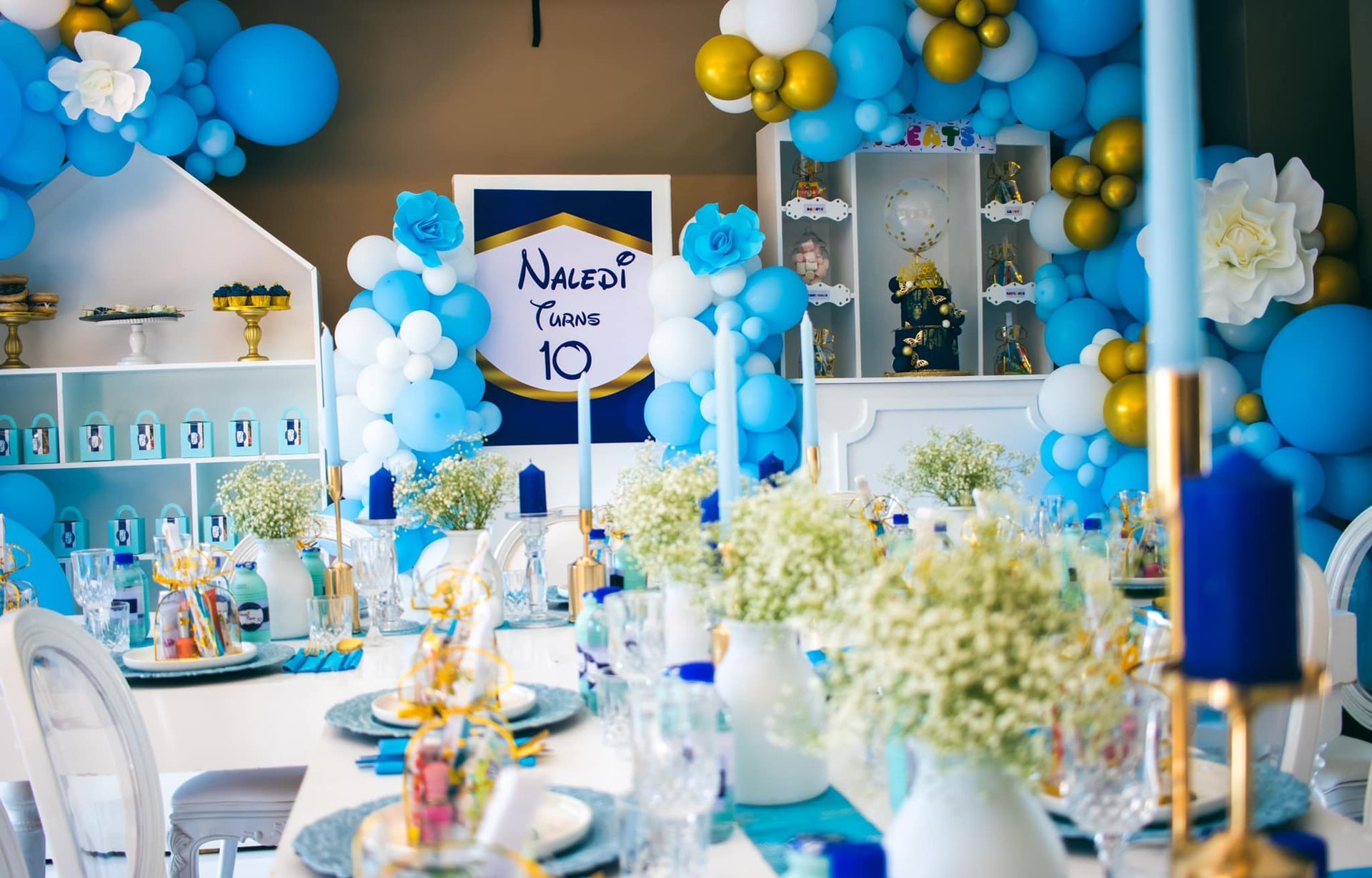 A table set for a birthday party with blue and gold balloons.