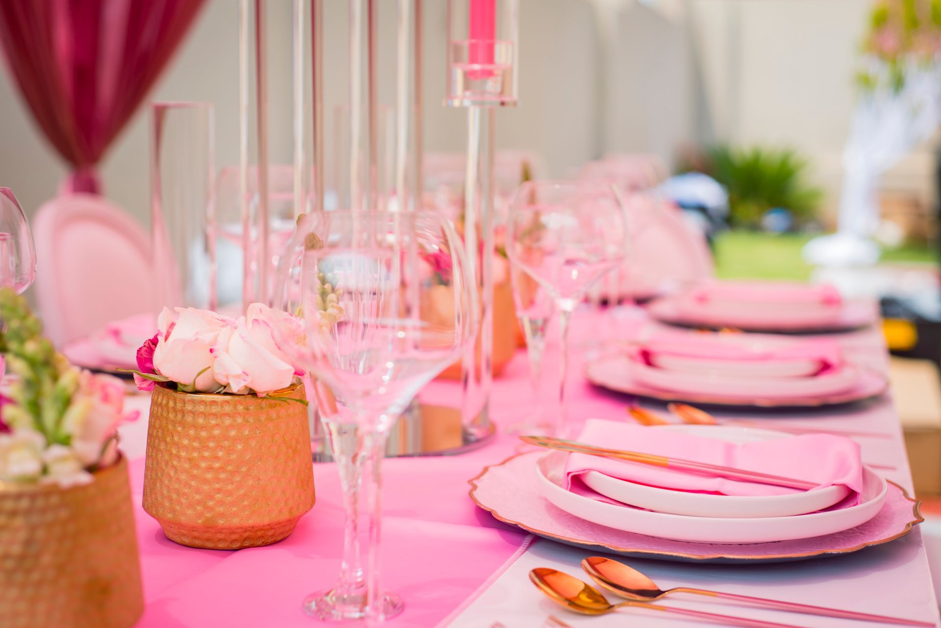 A table set for a wedding reception with pink plates , glasses , and silverware.