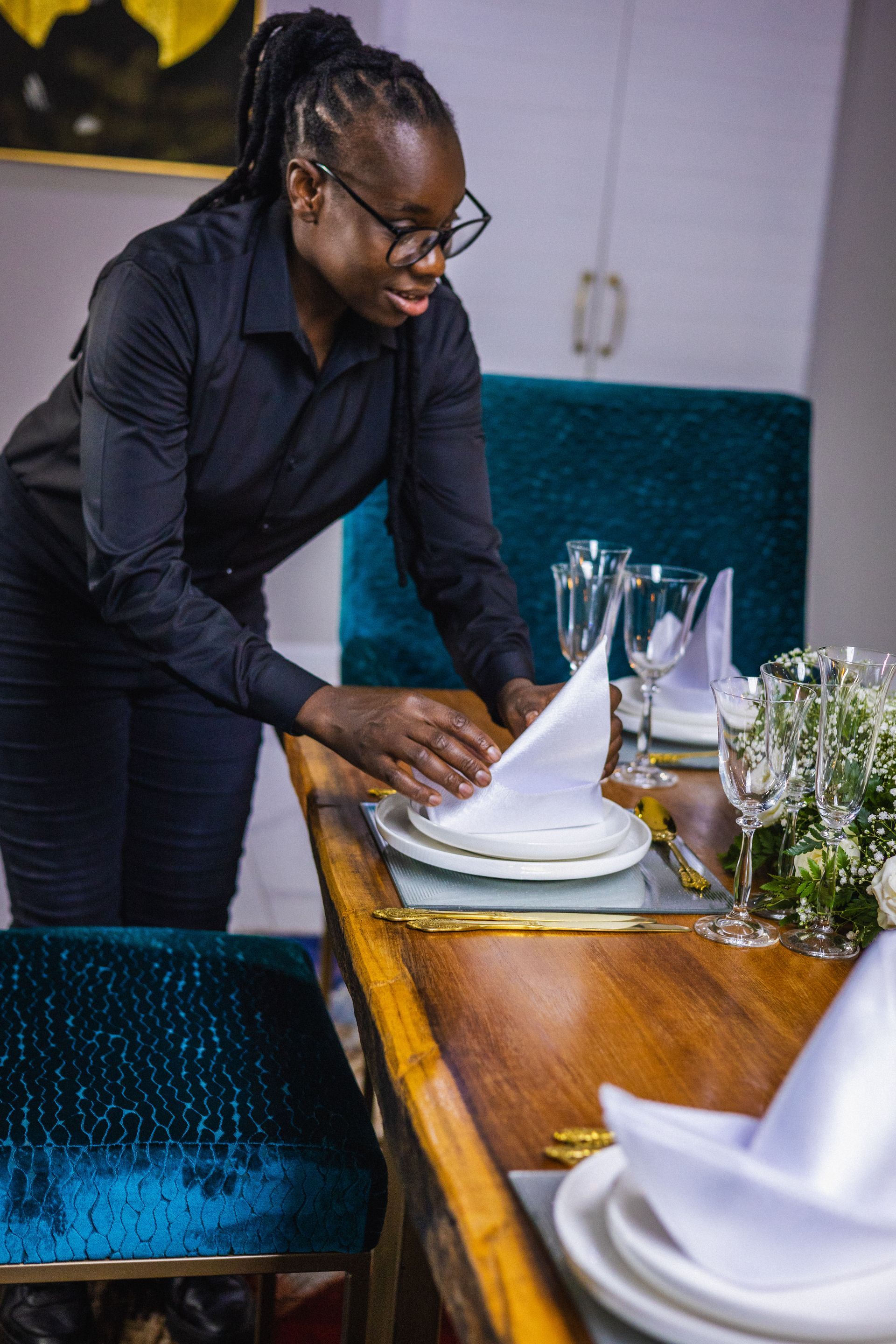 A woman is setting a table with plates , glasses , and napkins.