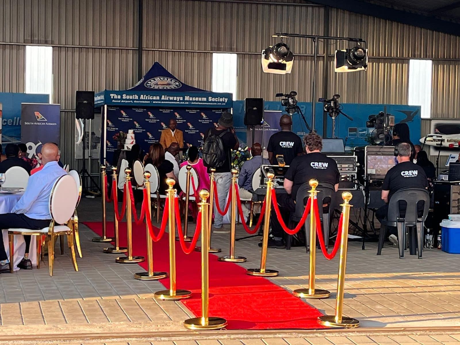 A group of people are sitting at tables in a room with a red carpet.