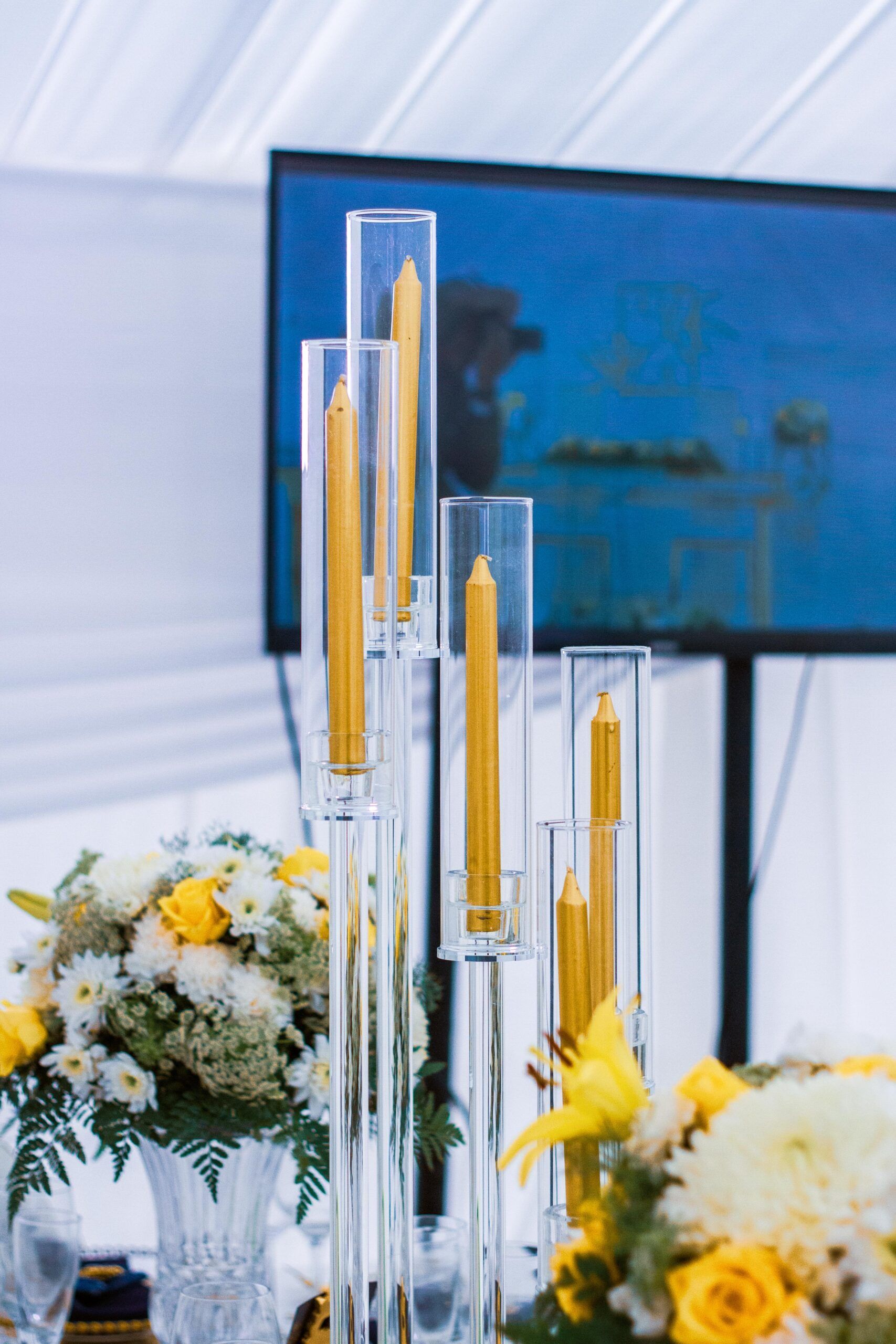 A table with flowers and candles on it and a television in the background.