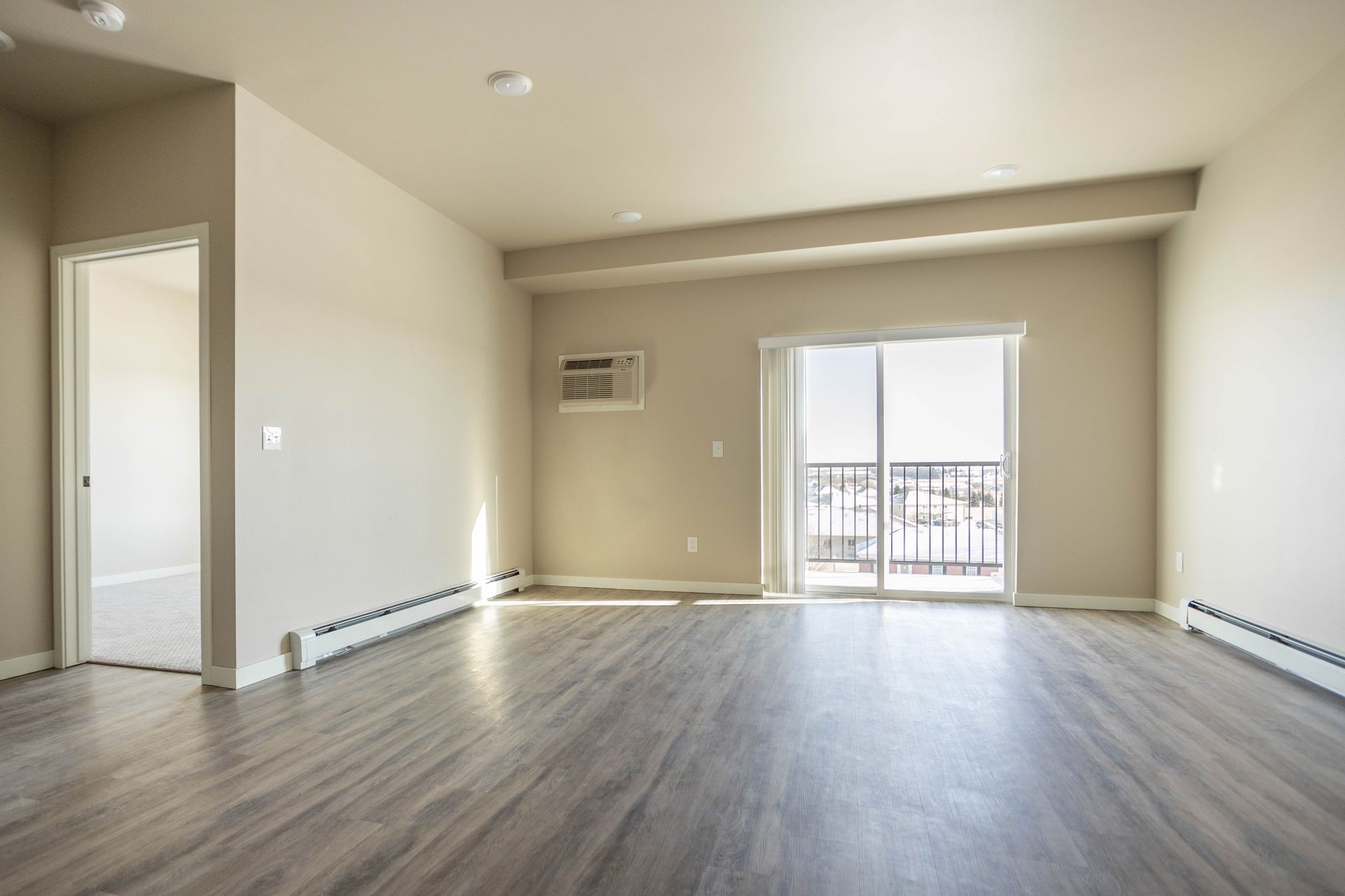 An empty living room with hardwood floors and sliding glass doors.