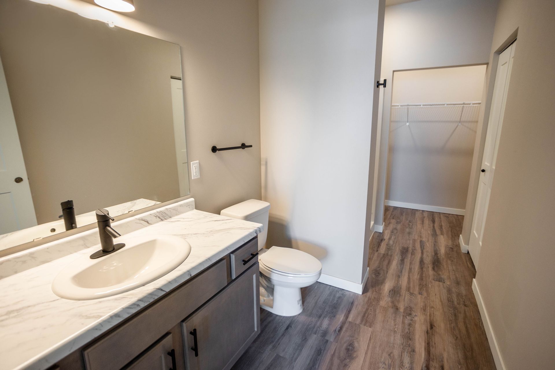 A bathroom with a sink , toilet , mirror and walk in closet.