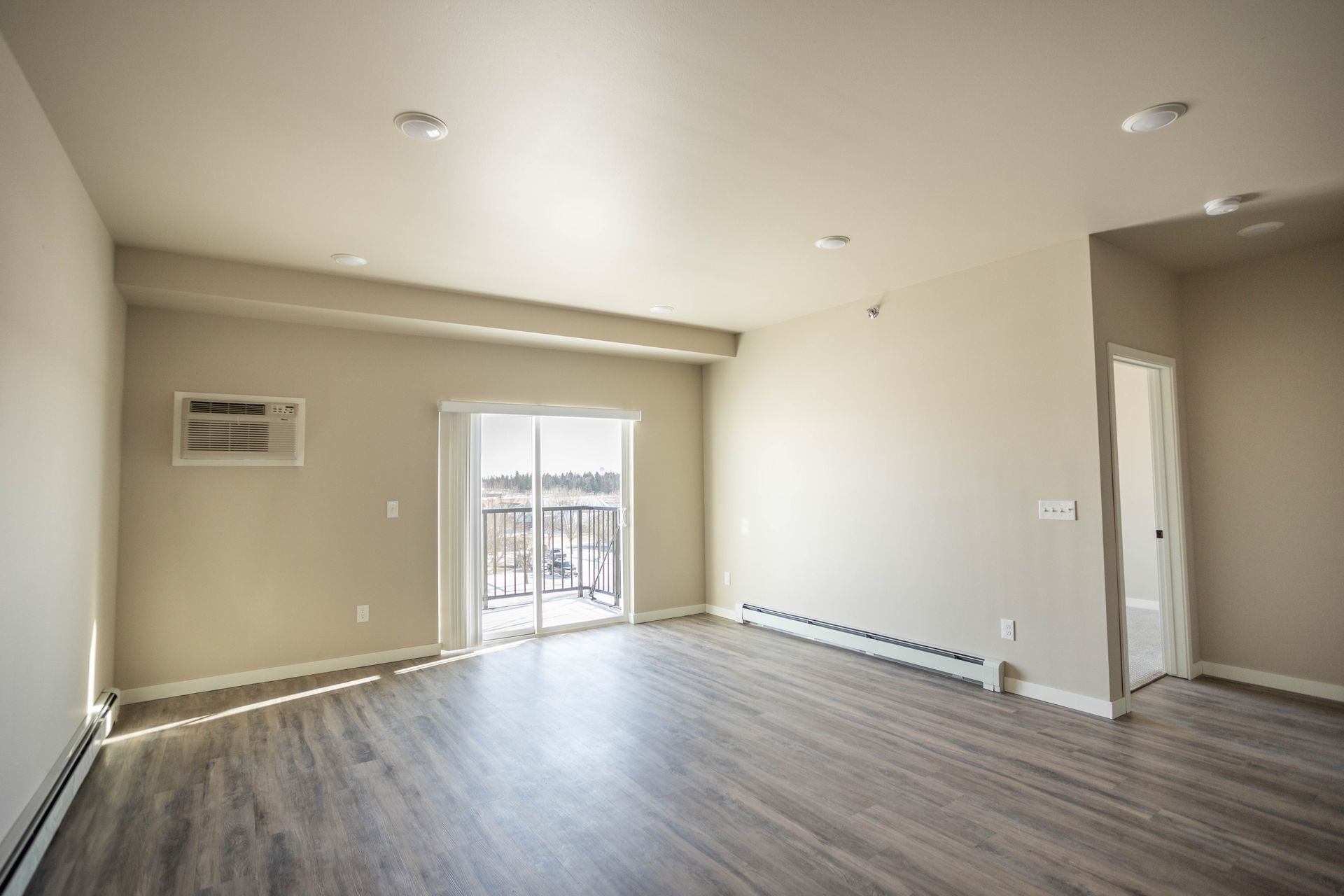 An empty living room with hardwood floors and sliding glass doors.