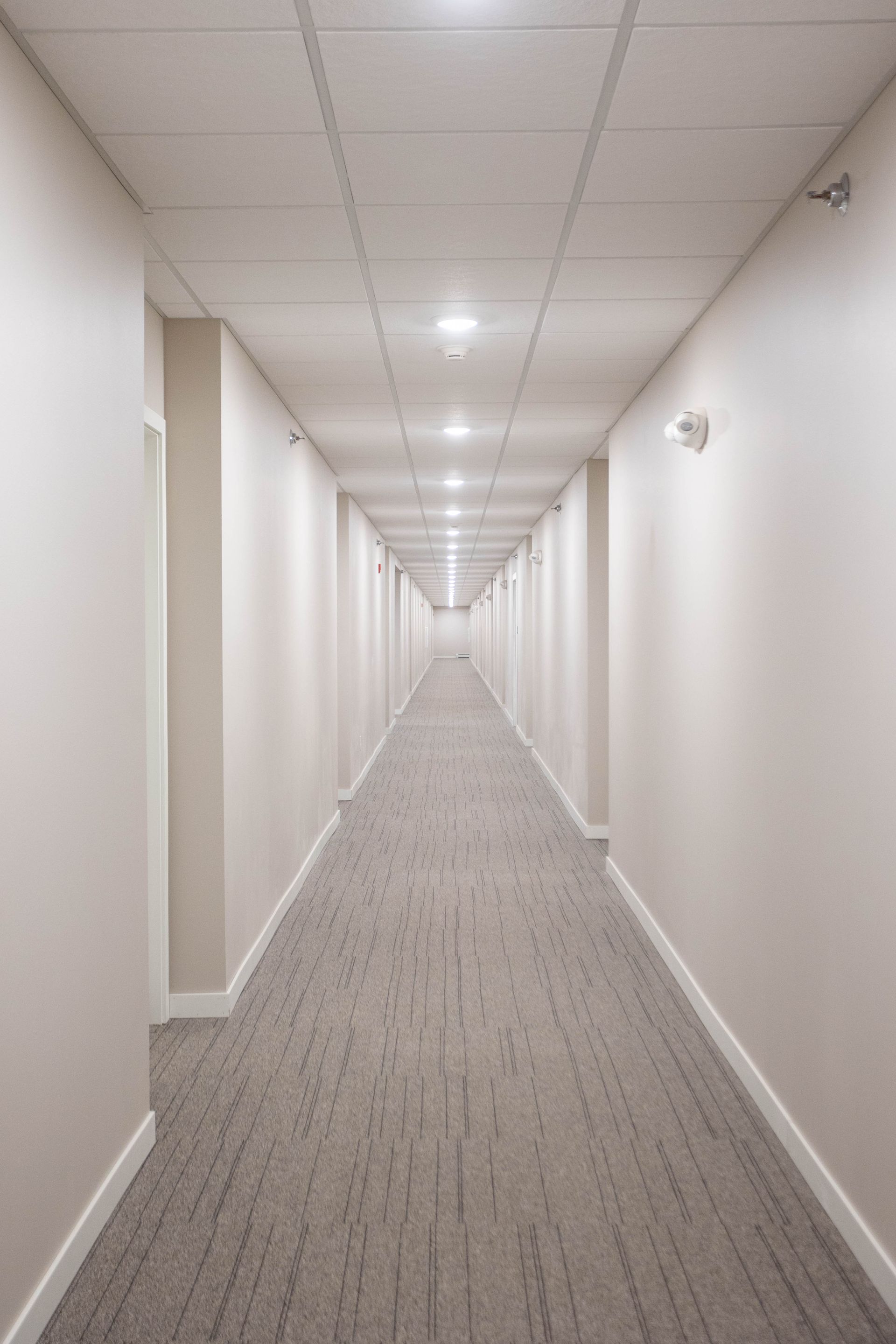 A long hallway with a carpeted floor and white walls in a building.