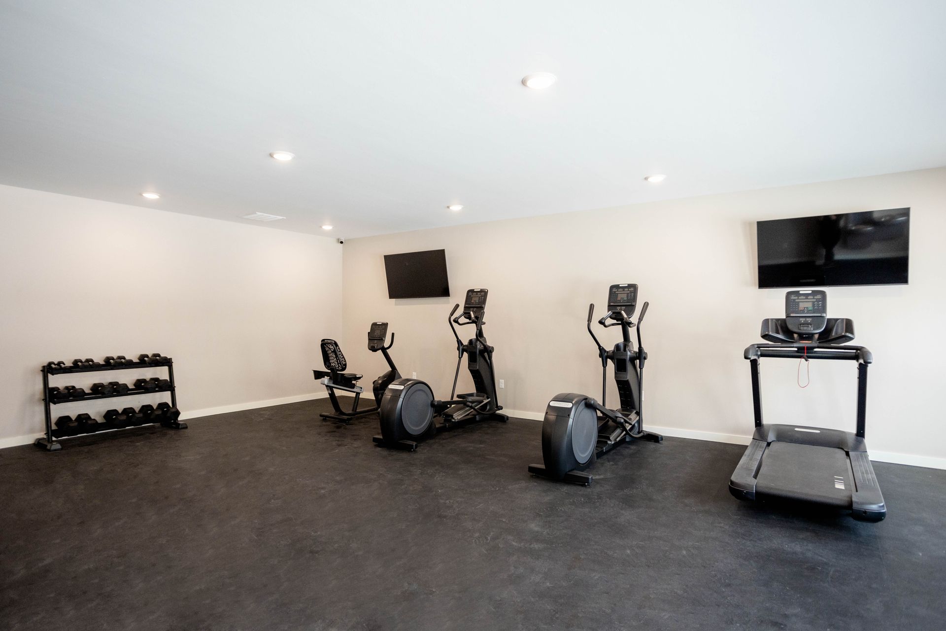A gym with a treadmill , elliptical , and dumbbell rack.