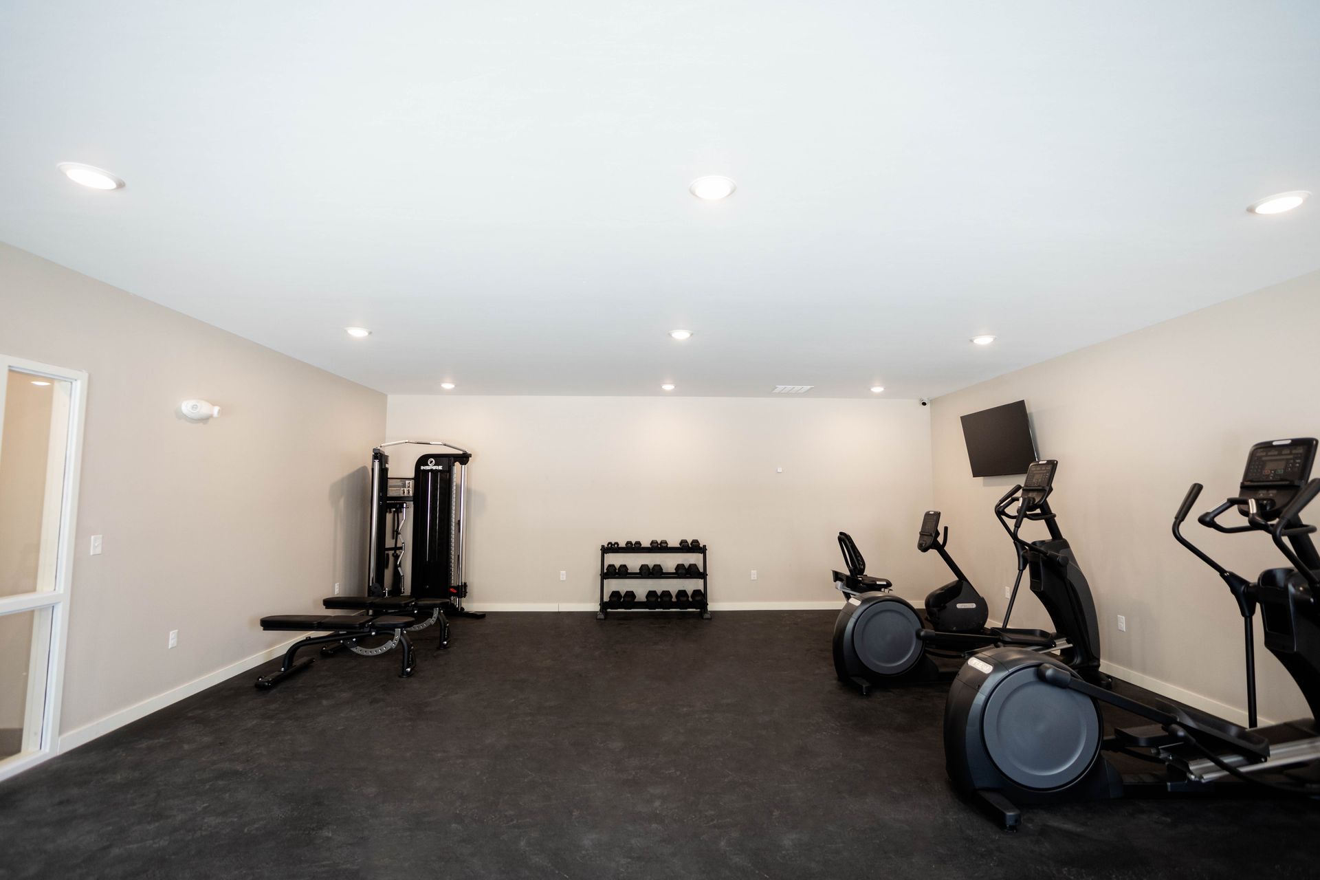 A gym with a lot of exercise equipment and a tv on the wall.