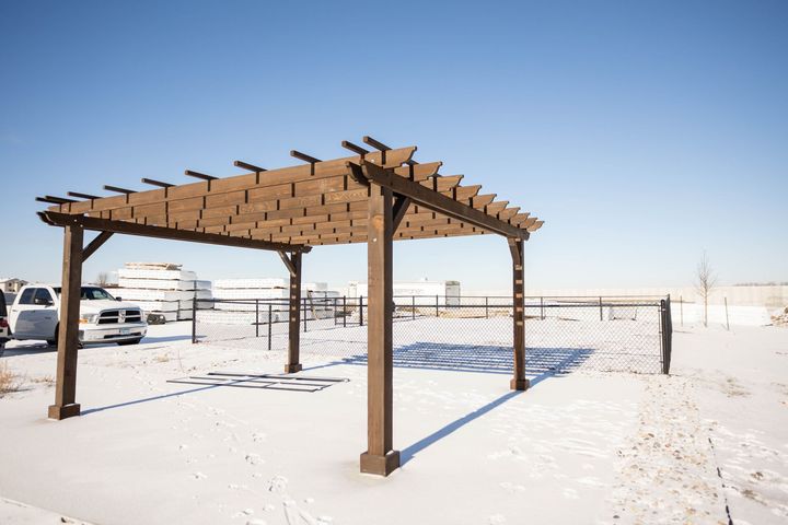 A pergola is sitting in the middle of a snowy field.