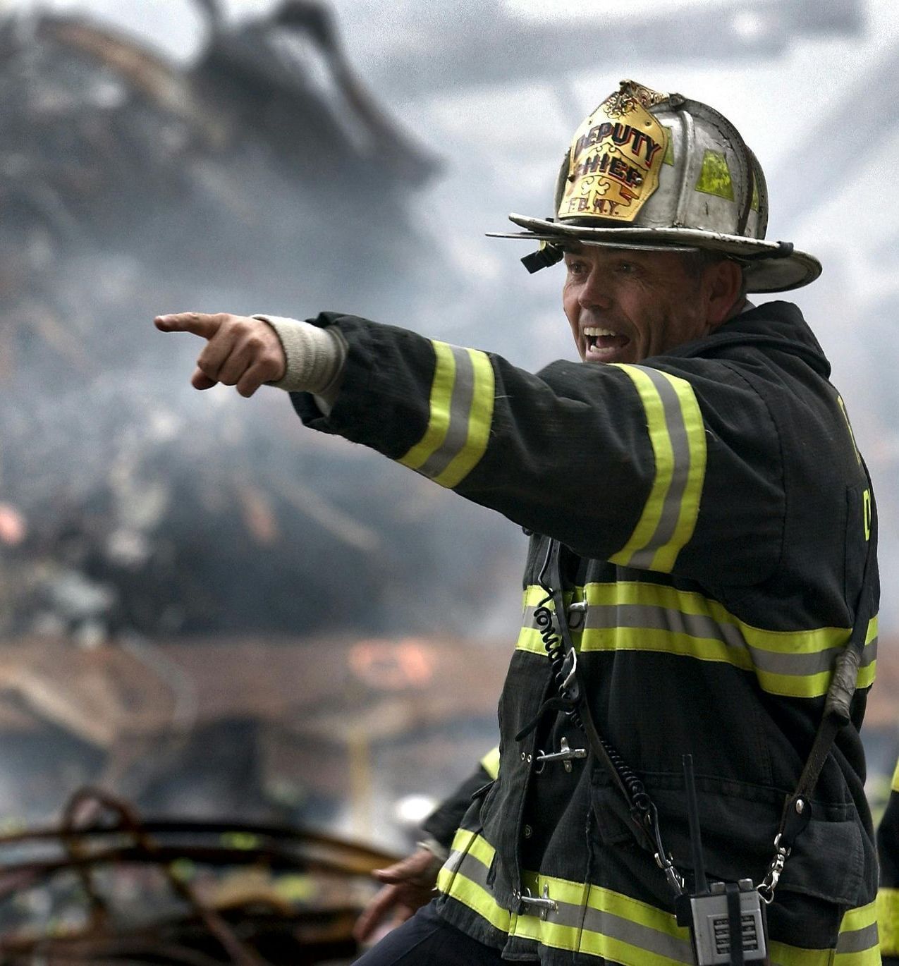 Firefighter pointing, face grim, amidst debris and smoke.