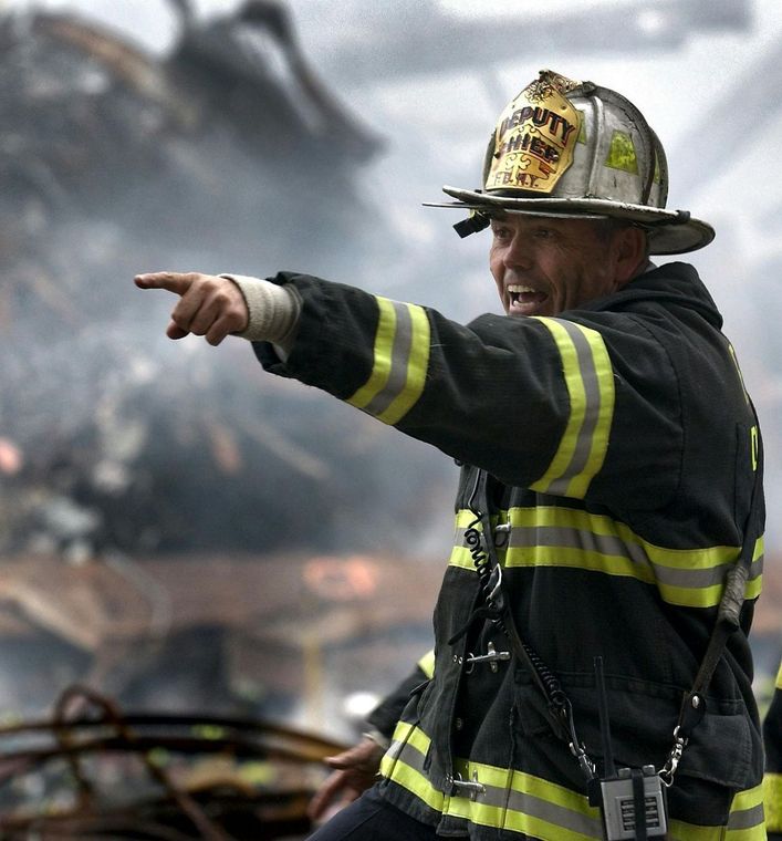 Firefighter pointing, face grim, amidst debris and smoke.