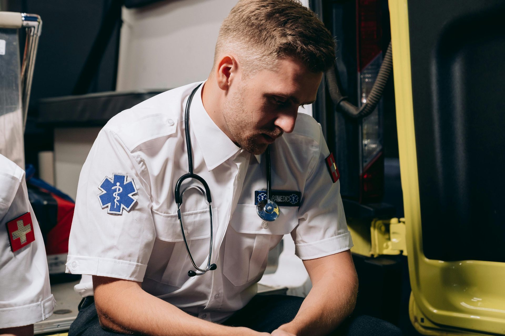 Paramedic in white uniform with stethoscope, looking down in ambulance.