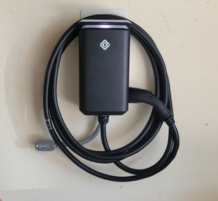 Black Rivian EV charger mounted on a beige garage wall, with a coiled charging cable.