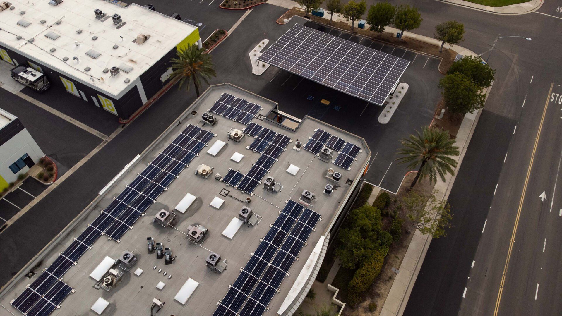 Aerial view of a building with solar panels on its roof and a solar-covered parking area.