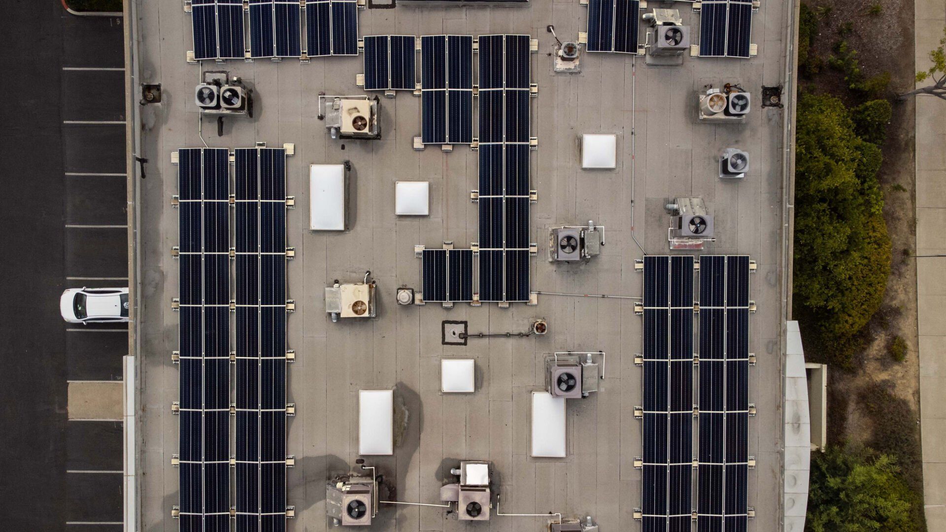 Overhead view of a flat roof with solar panels, HVAC units, and a parked car.