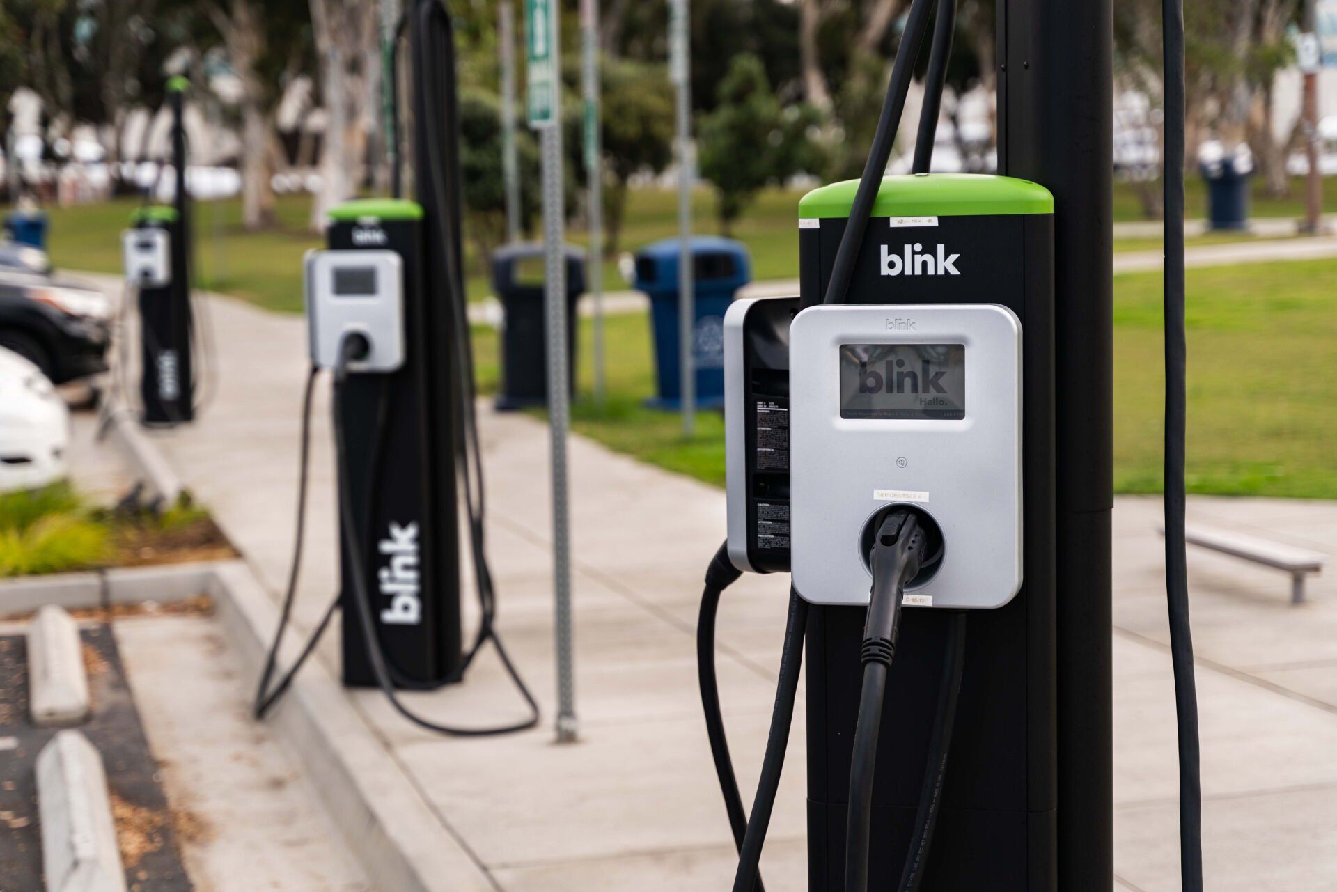 Row of black Blink electric vehicle charging stations along a sidewalk in a parking lot