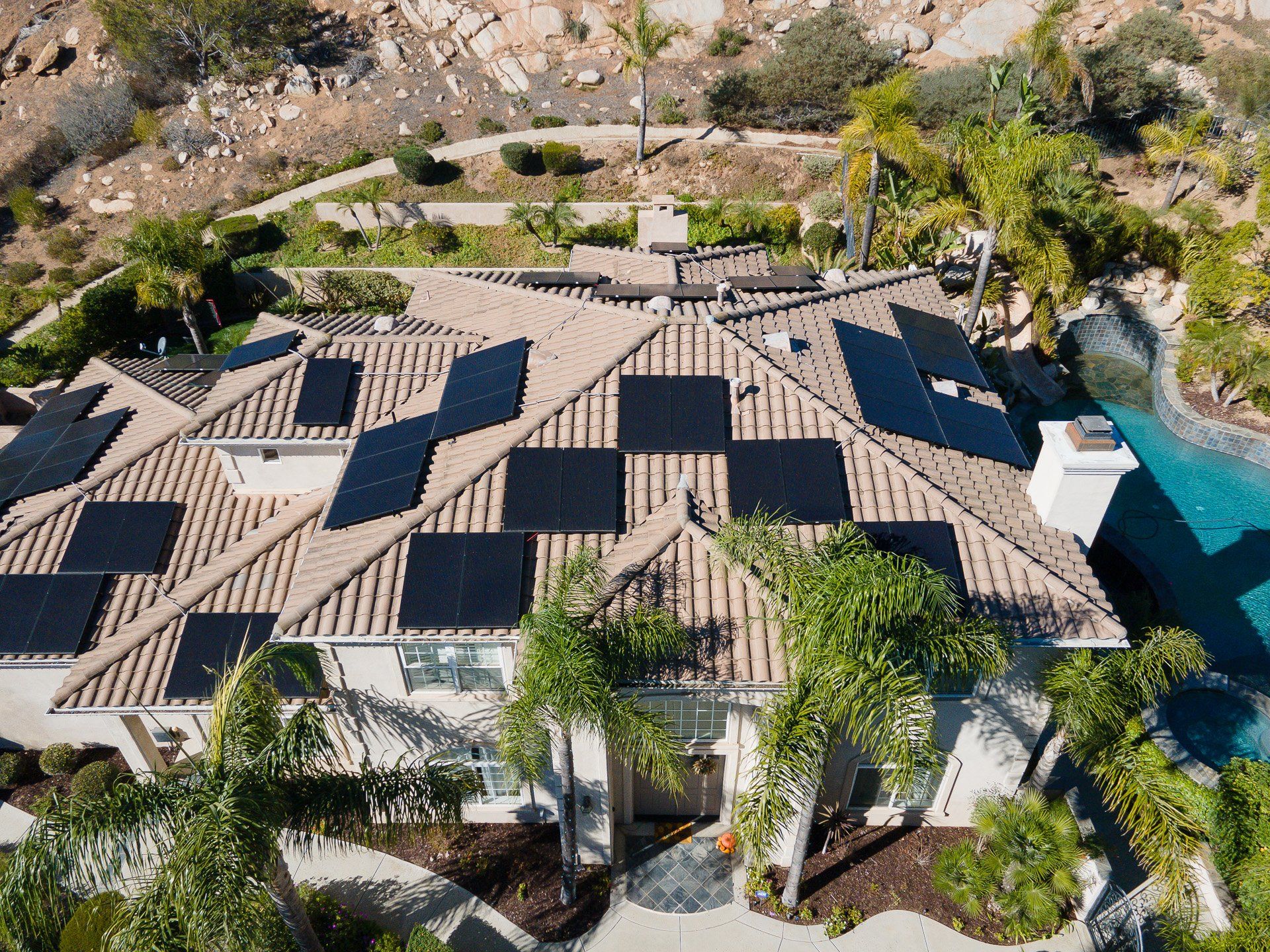 House with solar panels on the roof; poolside, surrounded by trees, set in a hilly landscape.