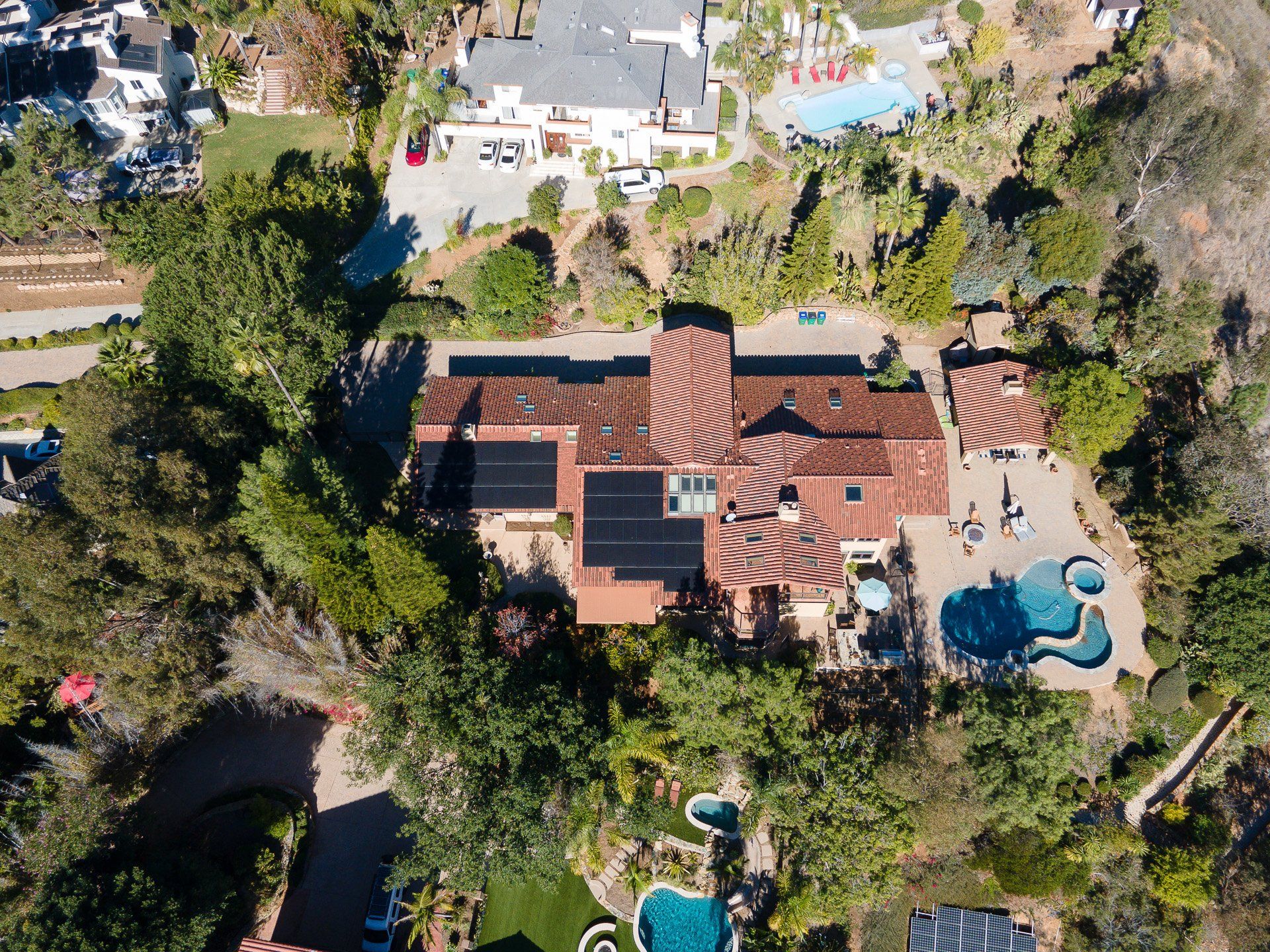 Aerial view of a large house with a red-tiled roof, solar panels, a pool, and surrounding greenery.