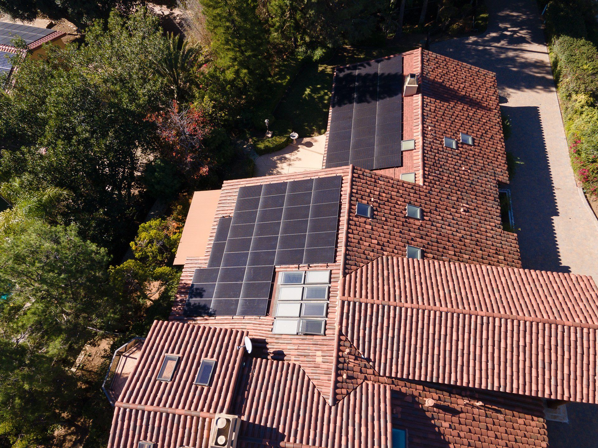 Overhead view of a house with red tile roof and black solar panels. Lush trees surround the house.