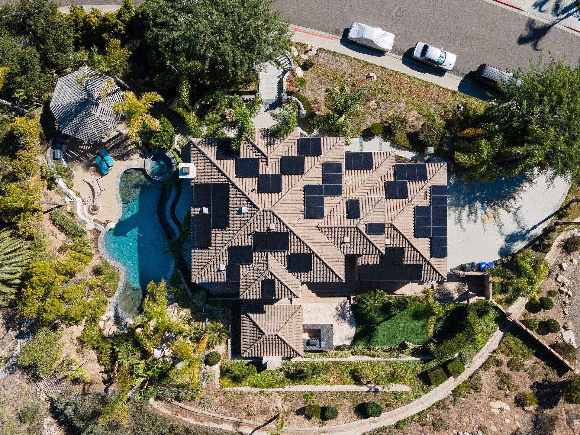 Aerial view of a house with solar panels, pool, and landscaping in a sunny setting.