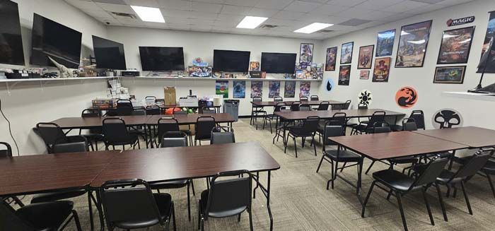 A room with tables and chairs, multiple screens, and posters, possibly a game store.