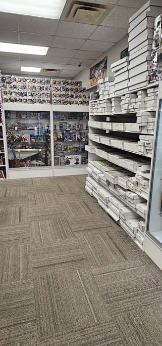 Inside a retail shop, displays with merchandise line the walls and shelving.  A carpeted floor is in the aisle.