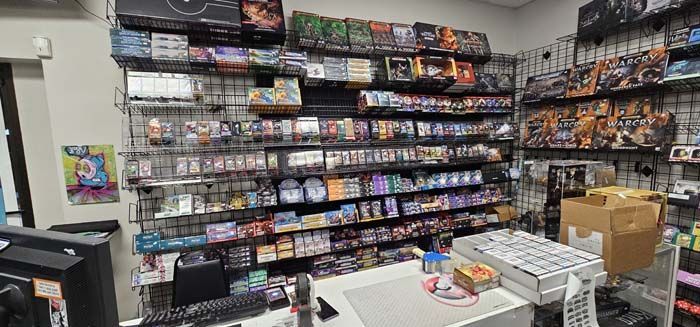 A retail store with shelves stocked with card games and collectibles behind a white counter.