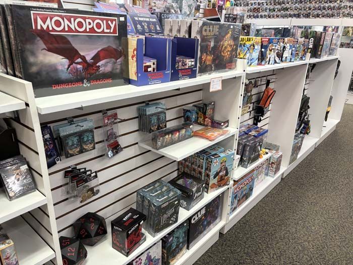Shelves of board games and card games in a store, including Monopoly, Gloomhaven, and dice.