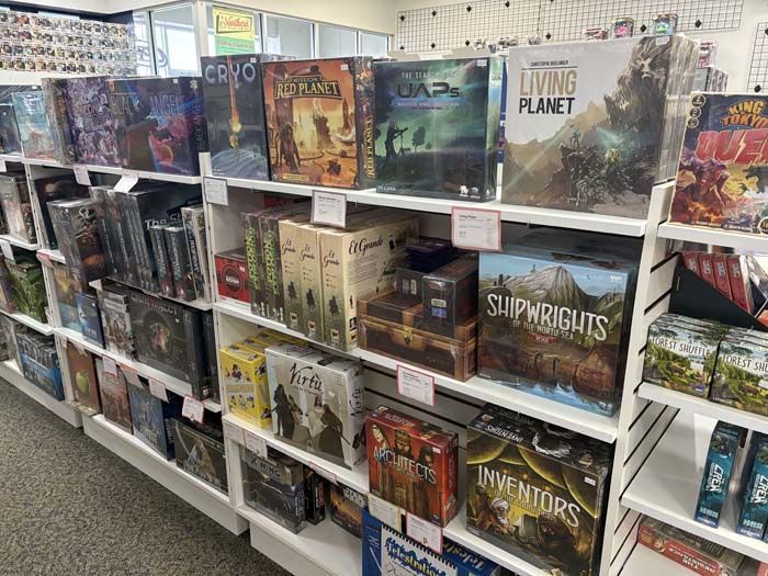 Board game shelves in a store, various boxes displayed, white shelves and walls.