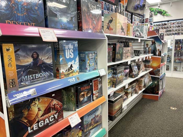 Board games displayed on shelves in a store, featuring titles like Mistborn and The Last of Us.