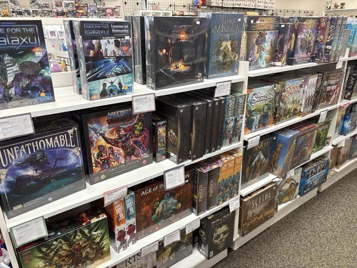 Shelves of board games in a store, various sizes and colors, white shelves.