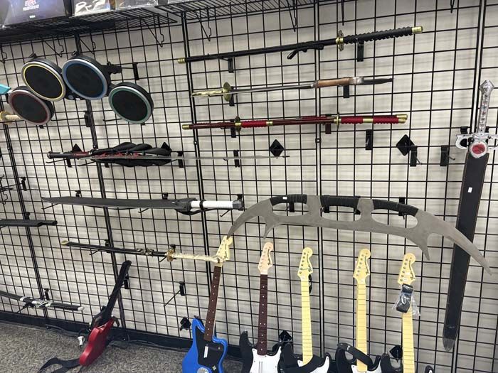 Swords and guitars displayed on a grid wall in a store. Various colors and styles of instruments and weapons.