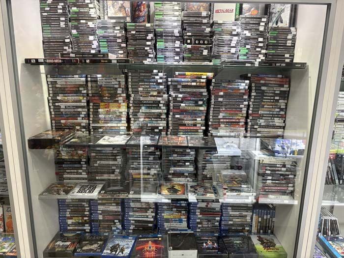 A display case filled with video games, primarily PS2, PS3, and PS4 titles, neatly organized on shelves.
