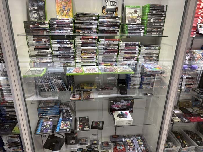 Glass display case filled with various video games, consoles, and accessories for sale.