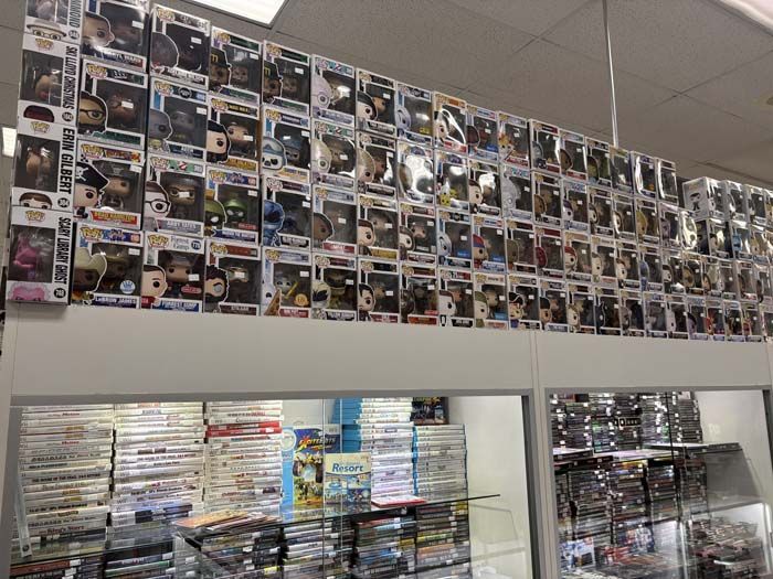 Wall of Funko Pop figures above glass display cases filled with video games.