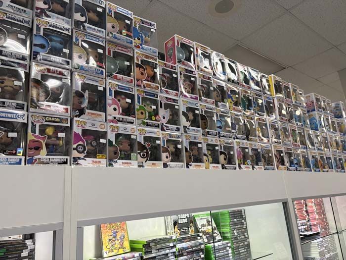 Shelf display of various Funko Pop figures in a store, with video games on a shelf below.