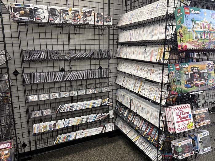 Shelves of video games in a store; black metal display, many game cases, some Lego sets visible.