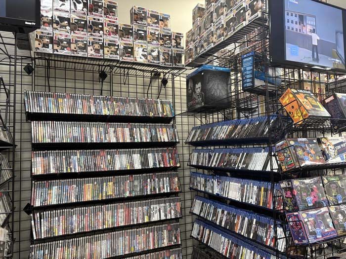 Shelves displaying DVDs and Blu-rays, with Funko Pop figures above. A TV plays a video.