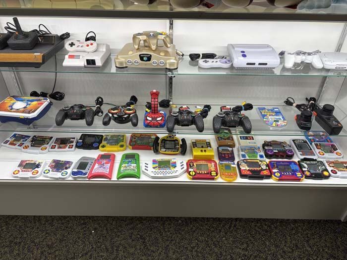 Display case with vintage video game consoles, controllers, and handheld games.