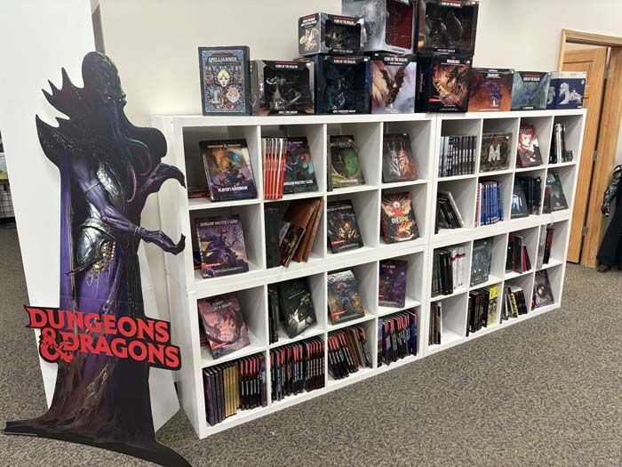 Dungeons & Dragons books displayed in white shelves with a cardboard cutout of a character.