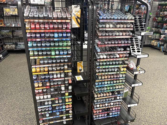Rows of hobby paints in a store, arranged by color on display shelves.