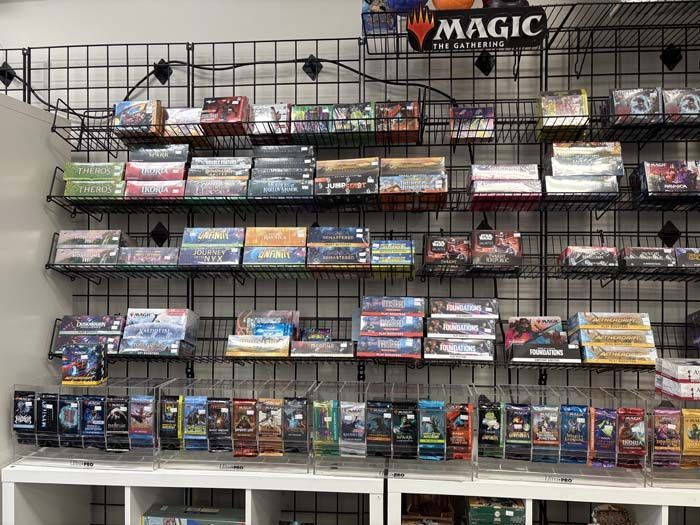 Shelves of board games and card game packs in a retail store. Black wire shelving. Various game boxes.