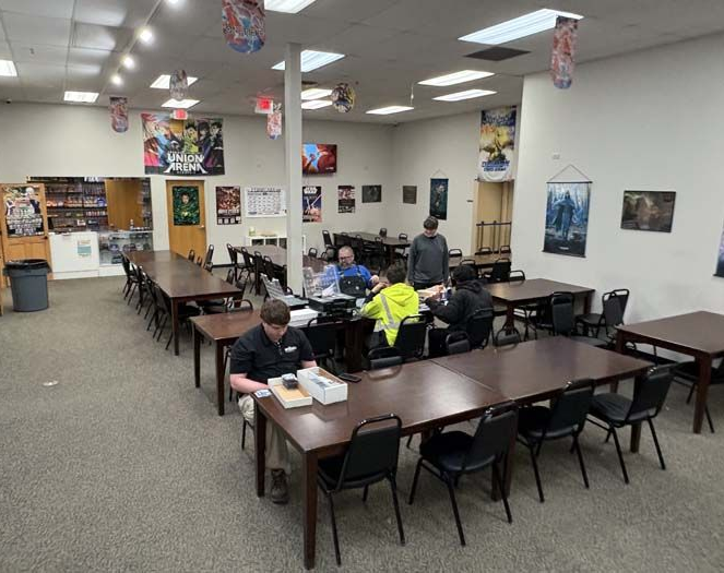 Game store interior with tables, people playing games, and game posters on the walls.